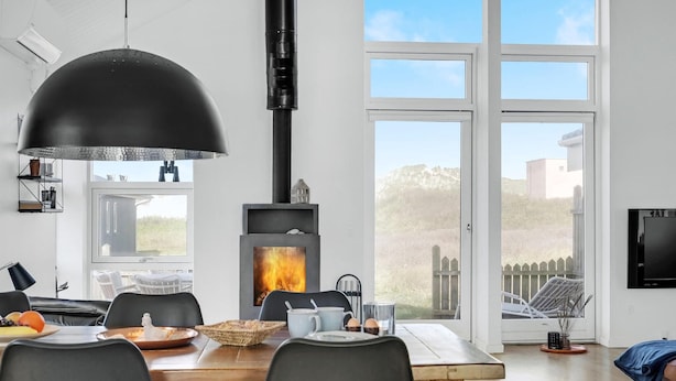 A modern kitchen with a large window, a fireplace, and a dining area with chairs and a table. - Pet friendly home in Blokhus with WiFi (Blokhus)