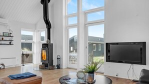 A modern living room with a fireplace, large windows, and a flat-screen TV. - Pet friendly home in Blokhus with WiFi (Blokhus)