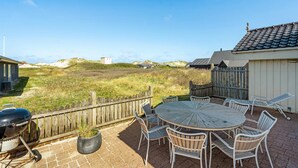 A patio with a round table and chairs, a barbecue grill, and a view of dunes and buildings in the distance. - Pet friendly home in Blokhus with WiFi (Blokhus)
