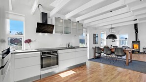 A modern kitchen with white cabinetry, a built-in oven, and a dining area with a large table and chairs. - Pet friendly home in Blokhus with WiFi (Blokhus)