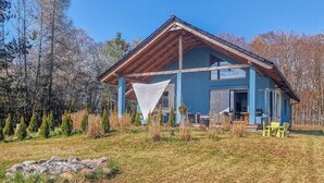 Une maison bleue avec un toit en bois, un porche abrité et un petit espace extérieur aménagé avec des chaises.