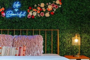 Una camera da letto con un neon che riporta la scritta “Life is Beautiful”, un letto con cuscini rosa e bianchi e un comodino con una lampada.