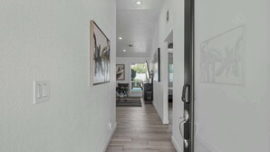 A hallway with wooden flooring, white walls, and several framed artworks. - Spring Song: Location, Style, Pool, Firepit, BBQ! (Scottsdale)