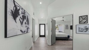 A hallway leading to a bedroom with a bed, a ceiling fan, and a door. - Spring Song: Location, Style, Pool, Firepit, BBQ! (Scottsdale)