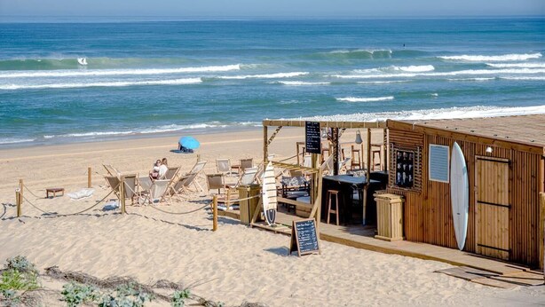 A beachside wooden structure with beach chairs, a surfboard, and a signboard.