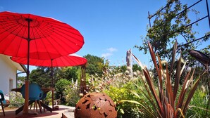 A wooden deck with a red umbrella, a metal sculpture, and a variety of plants.