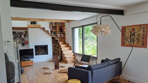 A modern living room with a sofa, a television, a bookshelf, a staircase, and a large window.