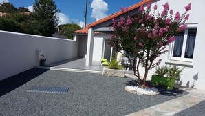 A residential area with a paved driveway, a small tree with pink flowers, and a white building with a red roof. - Vacation home in Meschers quiet area (Meschers-sur-Gironde)