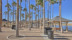 Un parco con palme, panchine, cestini e padiglioni gazebo lungo un corso d'acqua.