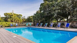 Une piscine rectangulaire avec une terrasse en bois, entourée d’une clôture en métal et d’arbres.