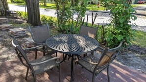 Une table ronde en métal, entourée de quatre chaises, et un patio pavé de briques.