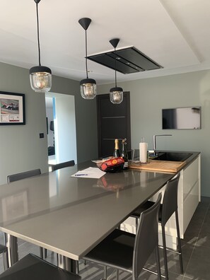 Une cuisine moderne dotée d’un grand îlot central, de luminaires suspendus, d’un téléviseur à écran plat et d’une photo encadrée accrochée au mur.