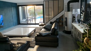 Ein modernes Wohnzimmer mit einer Couch, einem Couchtisch und einem Fernseher. Eine Treppe führt zu einem Balkon mit einem Pool.