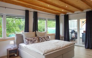A bedroom with a large bed, a nightstand, a lamp, and a view of a pool and outdoor area through large windows. - Lovely home in Schmallenberg with WiFi (Schmallenberg)