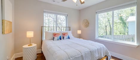 Un dormitorio con cama, ventilador de techo, ventana y mesita de noche.