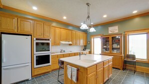 A kitchen with wooden cabinets, a white refrigerator, an oven, a sink, and a window with blinds.