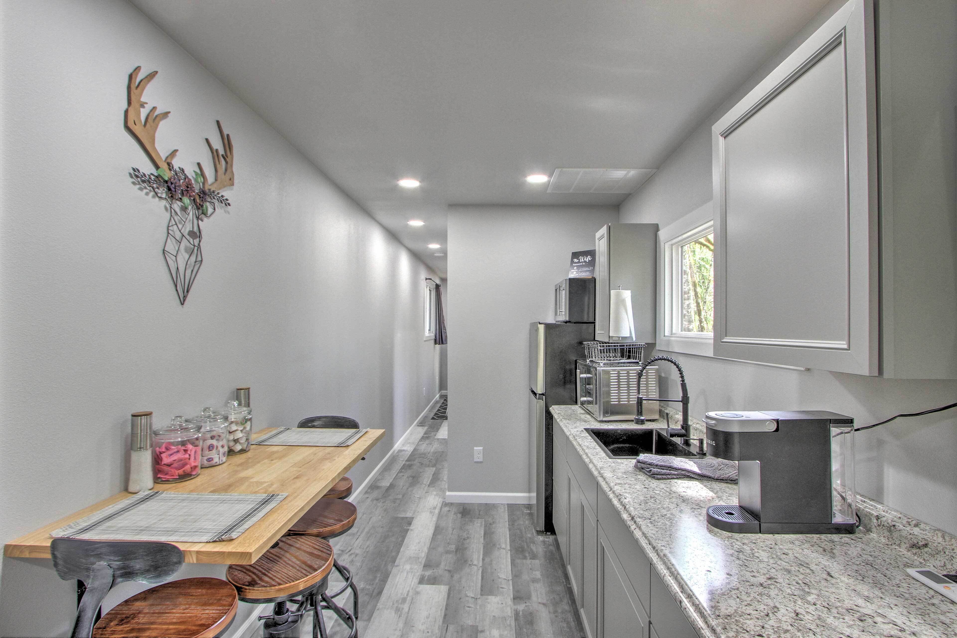 A modern kitchen with a wooden dining table, bar stools, a built-in oven, and a coffee machine.