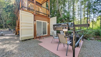 Une cabane dotée d’une terrasse, d’un espace salon extérieur et d’un barbecue.