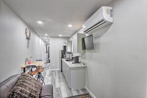 A narrow hallway with a kitchenette, a seating area with a couch and a coffee table, and a mounted TV on the wall.