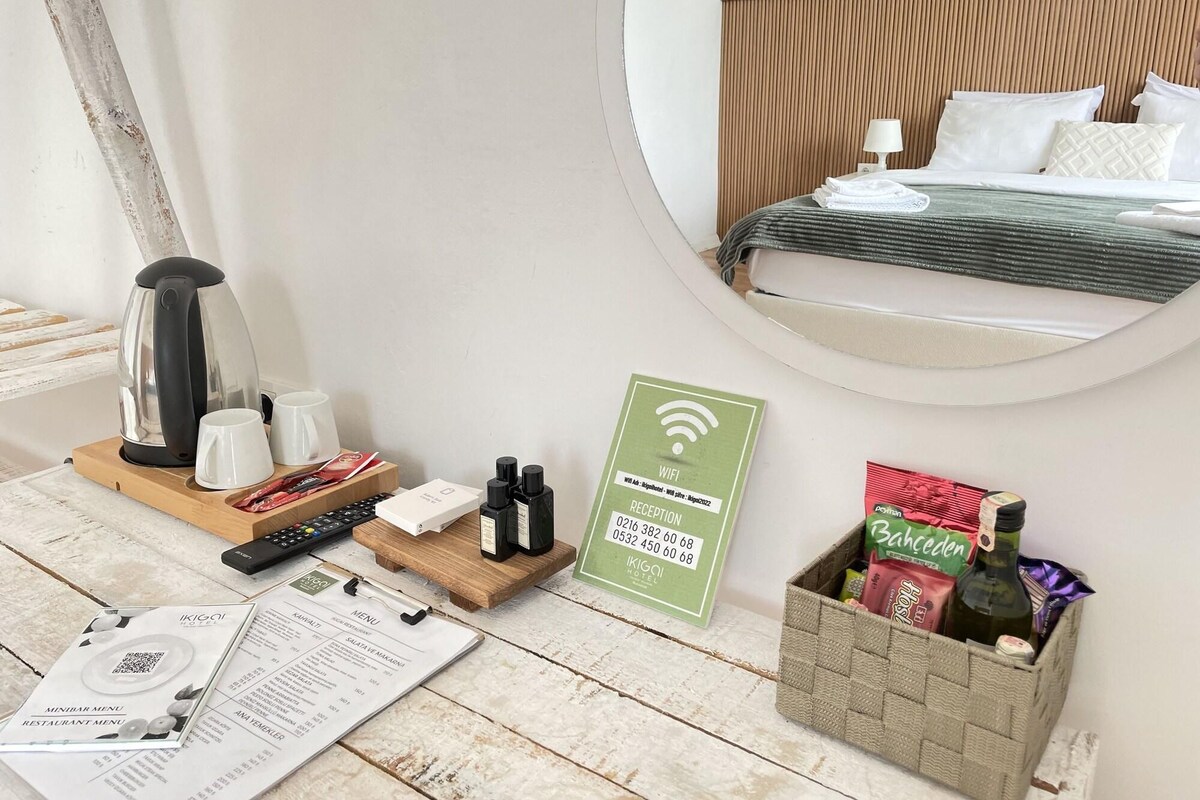 A hotel room with a bed, a coffee maker, a remote control, a Wi-Fi sign, a reception sign, a menu, and a basket of snacks.