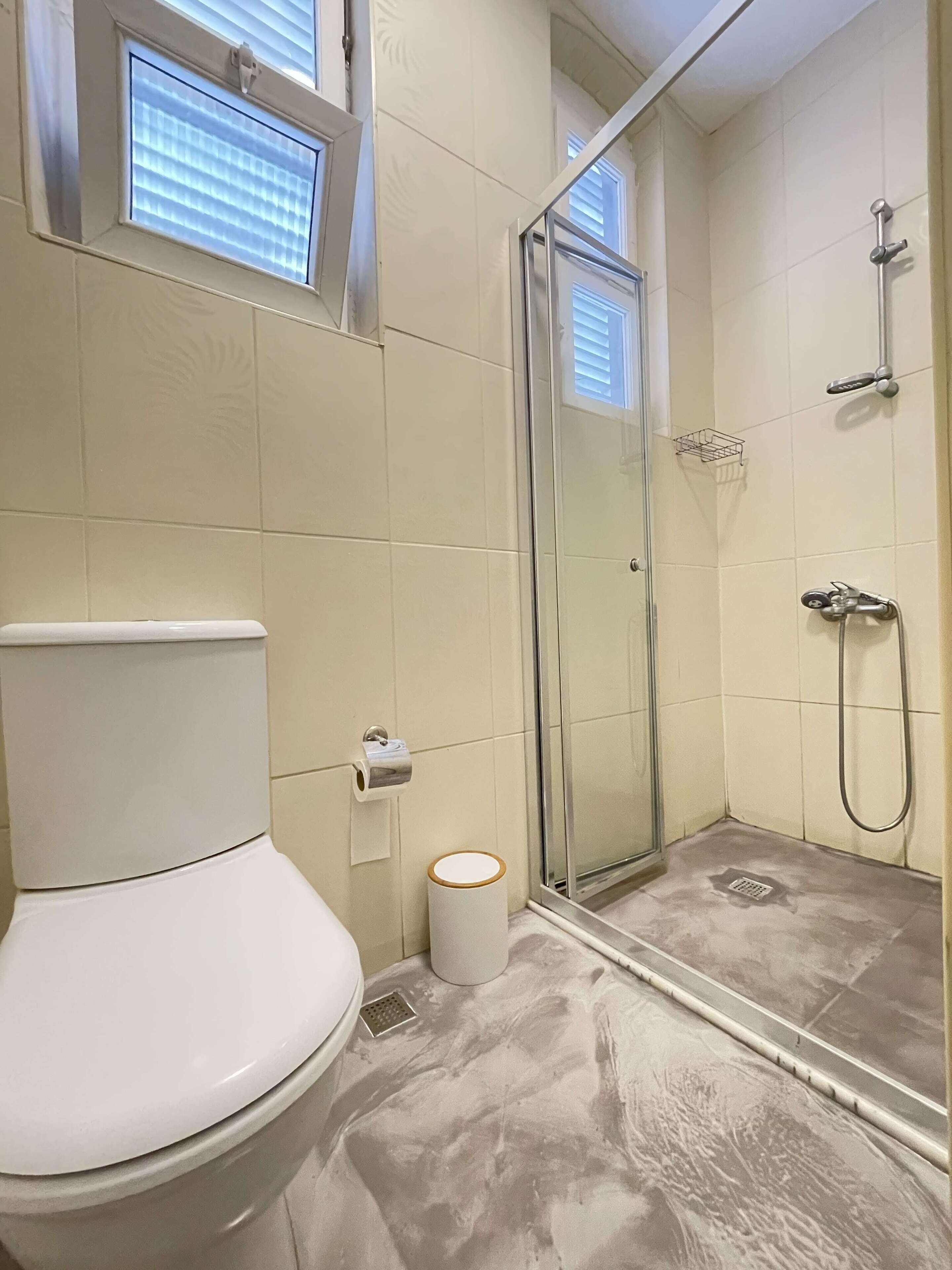 A bathroom with a toilet, a glass-enclosed shower, and a window above the toilet.