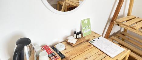 Une table en bois avec une bouilloire, des tasses, une télécommande et un menu. Un miroir reflète un lit avec des oreillers.