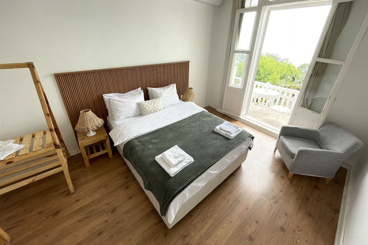 A bedroom with a wooden bed, a nightstand, a chair, and large windows.