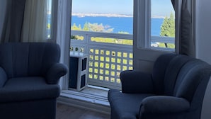 Ein Zimmer mit zwei dunkelblauen Sesseln, einem weißen Fenster mit Meerblick und einem weißen Geländer.