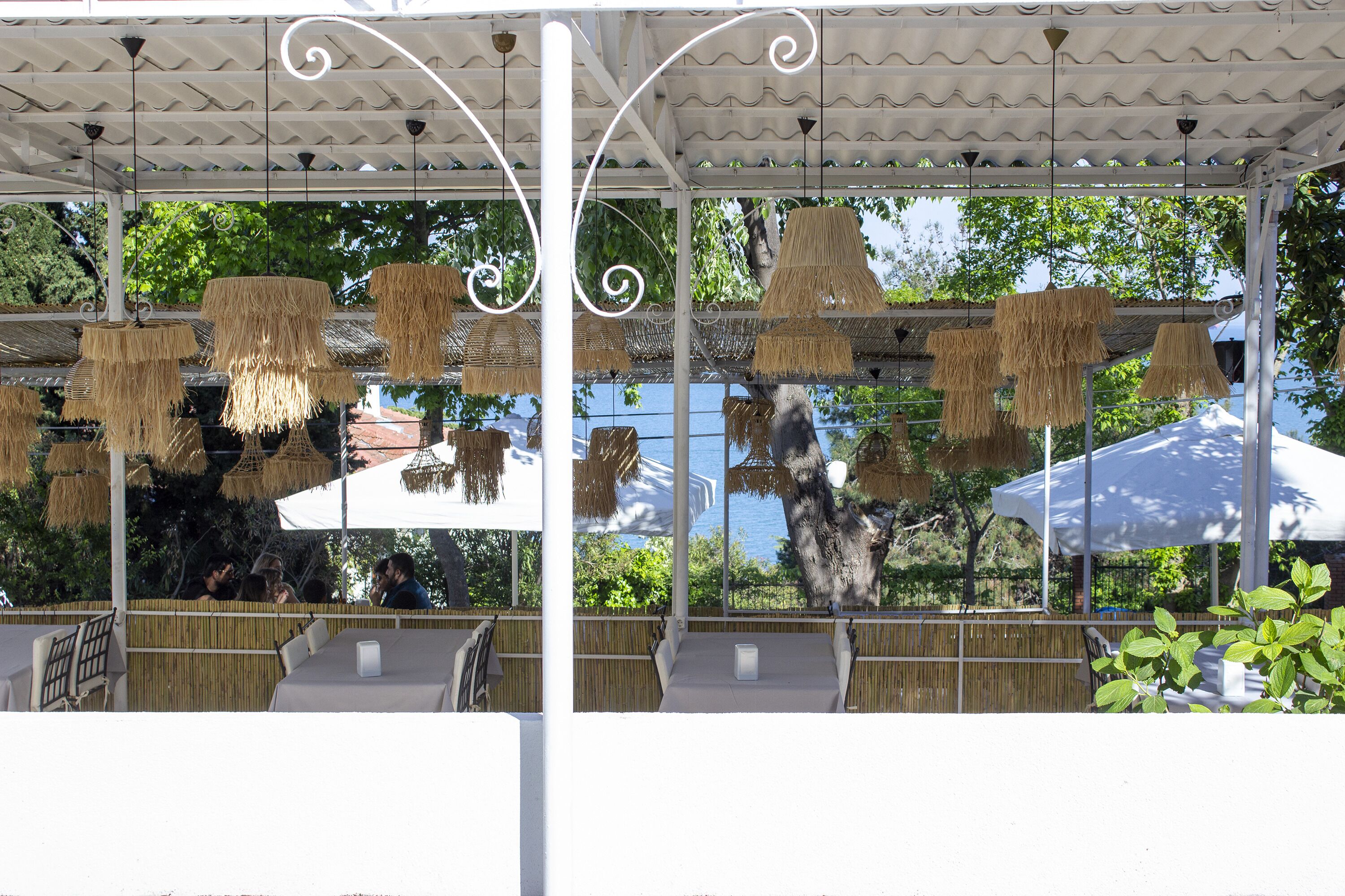 An outdoor seating area with tables and chairs, covered by a white canopy, and hanging thatched lamps.