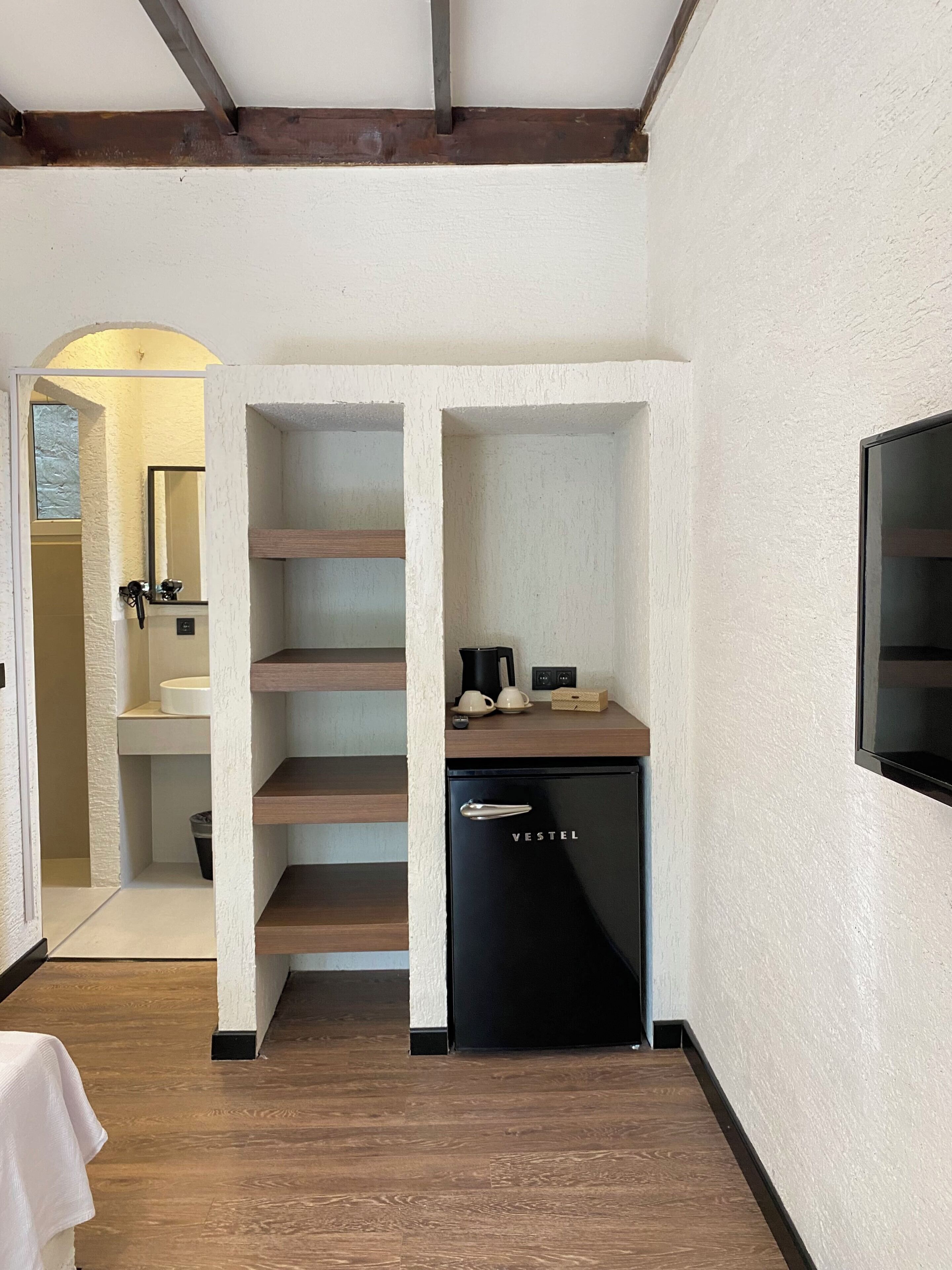 A compact kitchen with a black refrigerator, wooden shelves, and a white sink.