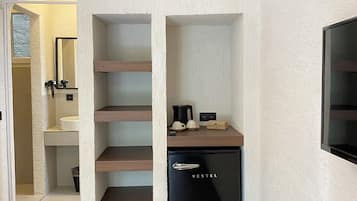 Una cocina compacta con un refrigerador negro, estantes de madera y un lavamanos blanco.
