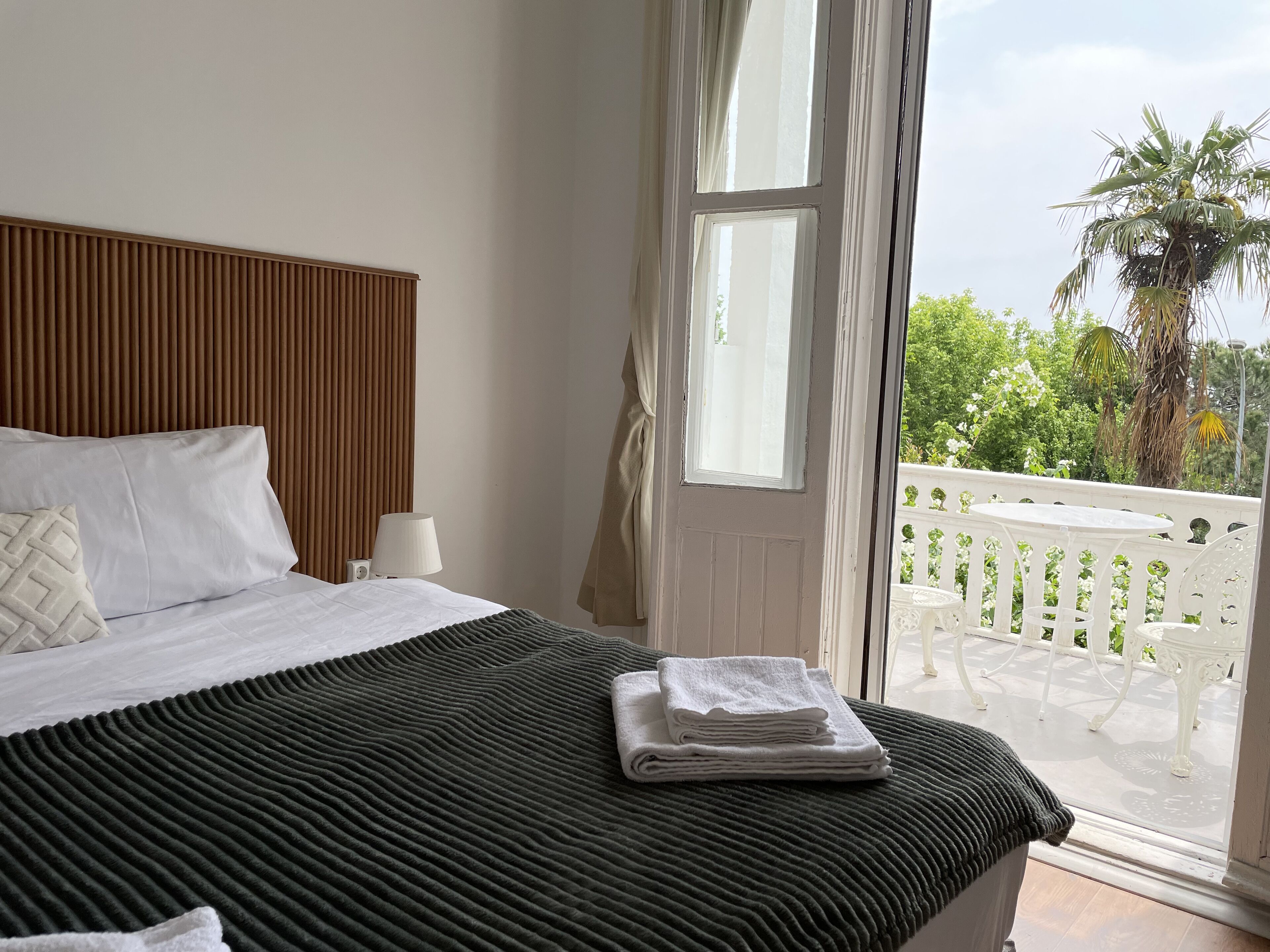 A bedroom with a bed, a window, and a view of a balcony with outdoor furniture.