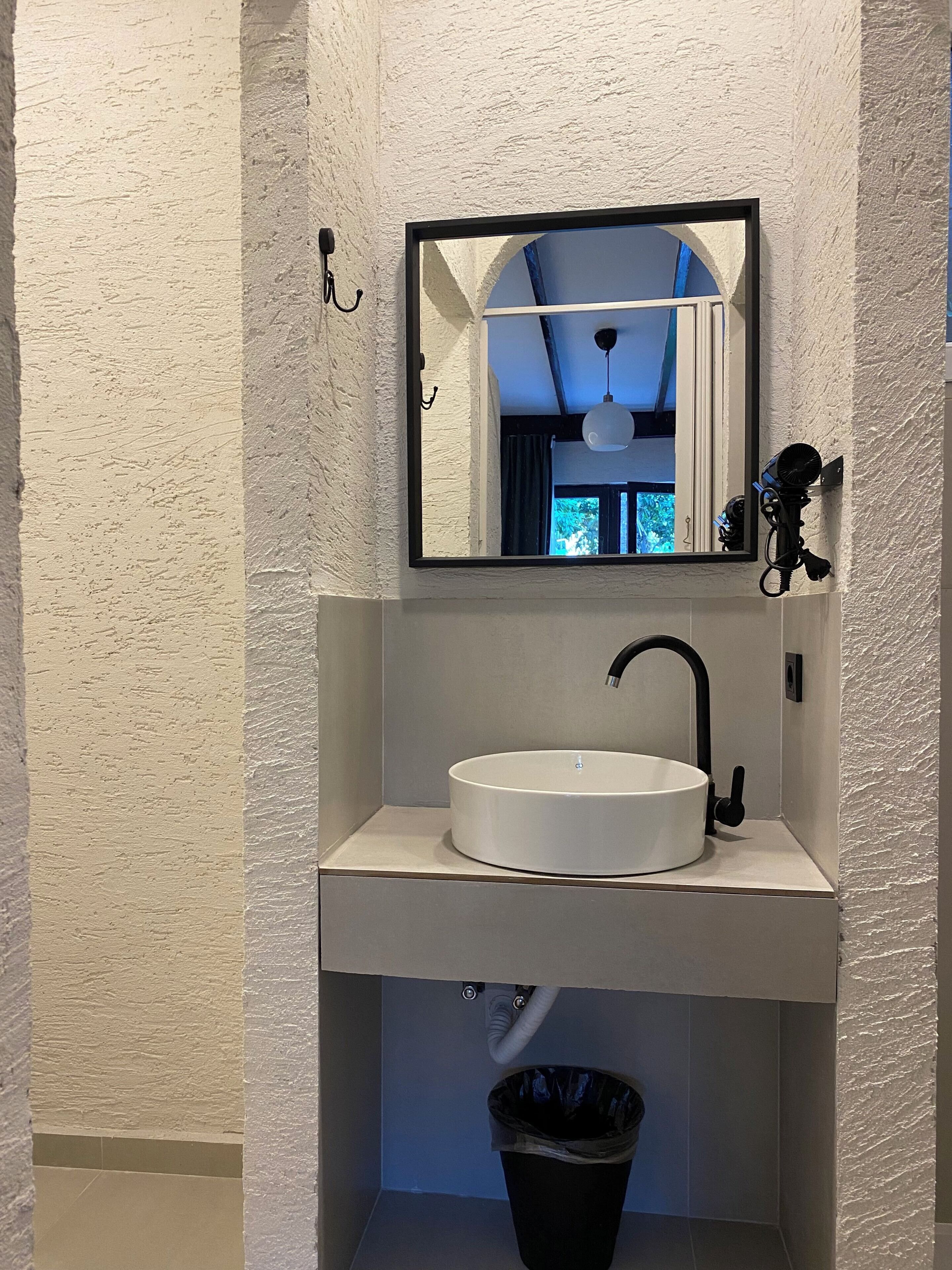 A bathroom with a white sink, a black faucet, a mirror, and a black trash bin.