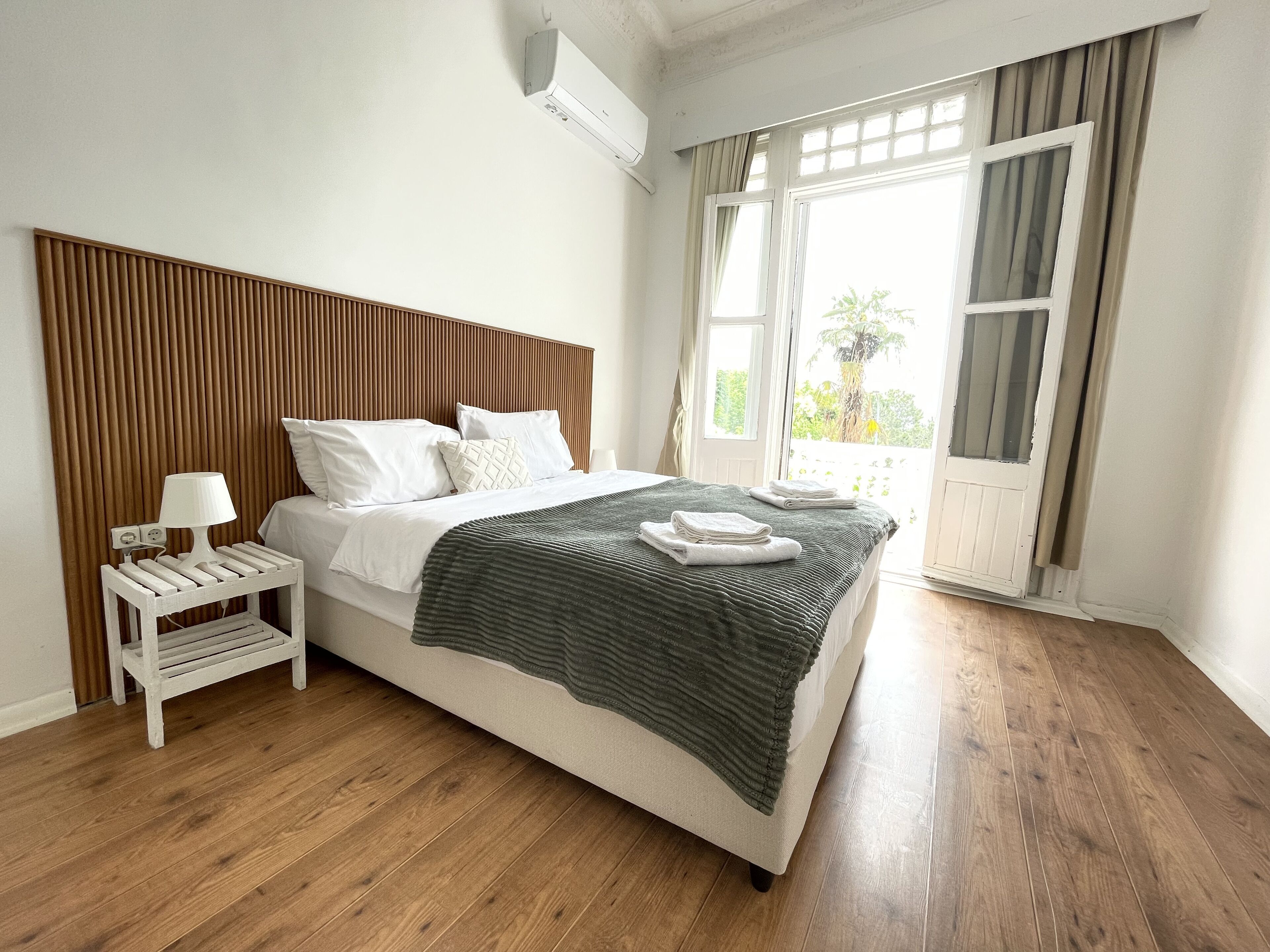 Un dormitorio con cama, mesita de noche con lámpara, ventana con cortinas y vistas al exterior.