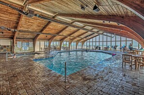 Una piscina interior amb sostre de fusta i paviment de maó, envoltada d'zones d'estar.
