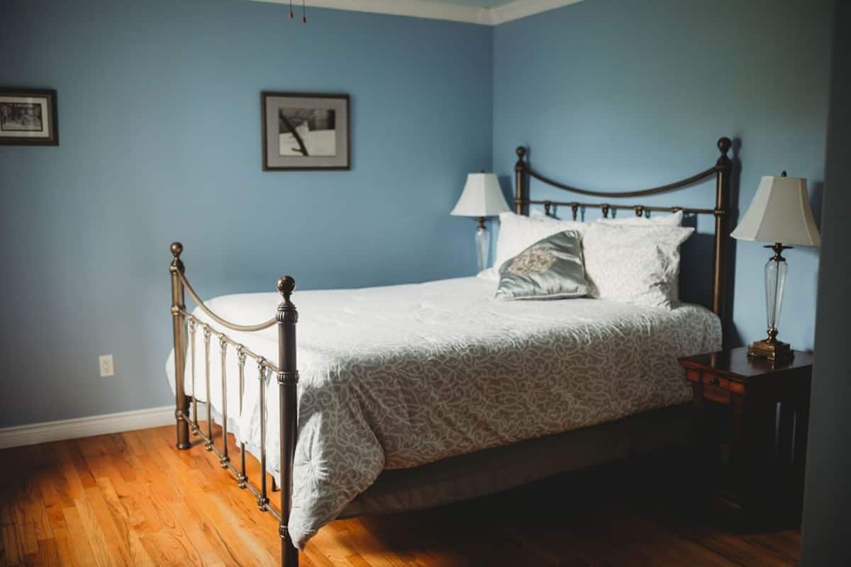 A bedroom with a four-poster bed, two bedside lamps, and a framed picture on the wall.