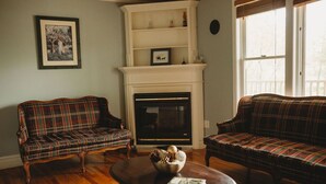 A living room with two plaid sofas, a fireplace, and a wooden coffee table. - The Carriage House Inn (Grand Falls - Windsor)