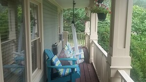 A porch with white railings, a hanging planter with flowers, and two blue chairs with striped cushions. - The Carriage House Inn (Grand Falls - Windsor)