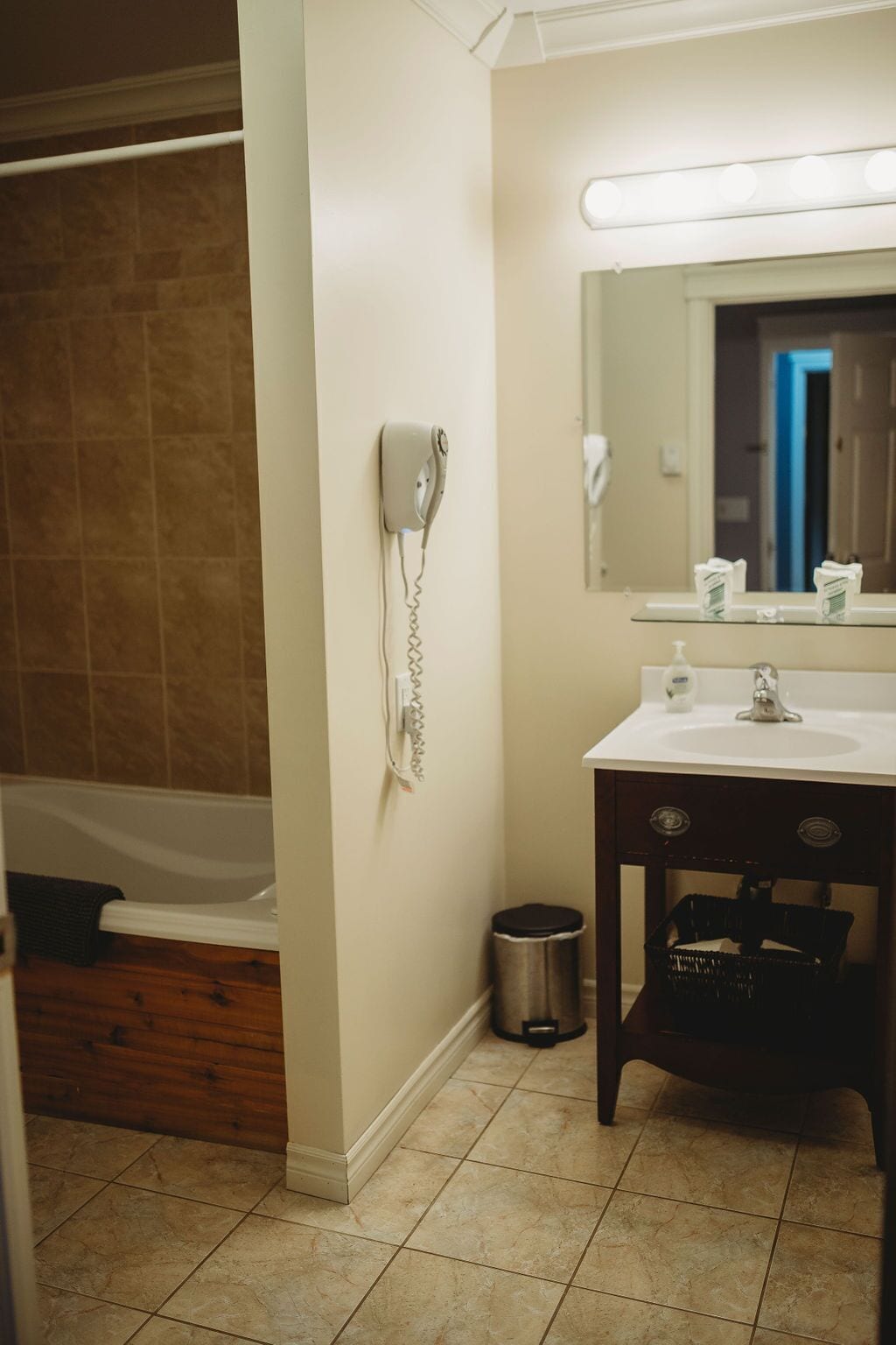 A bathroom with a white sink, a mirror, a hairdryer on the wall, a trash can, and a wooden floor.