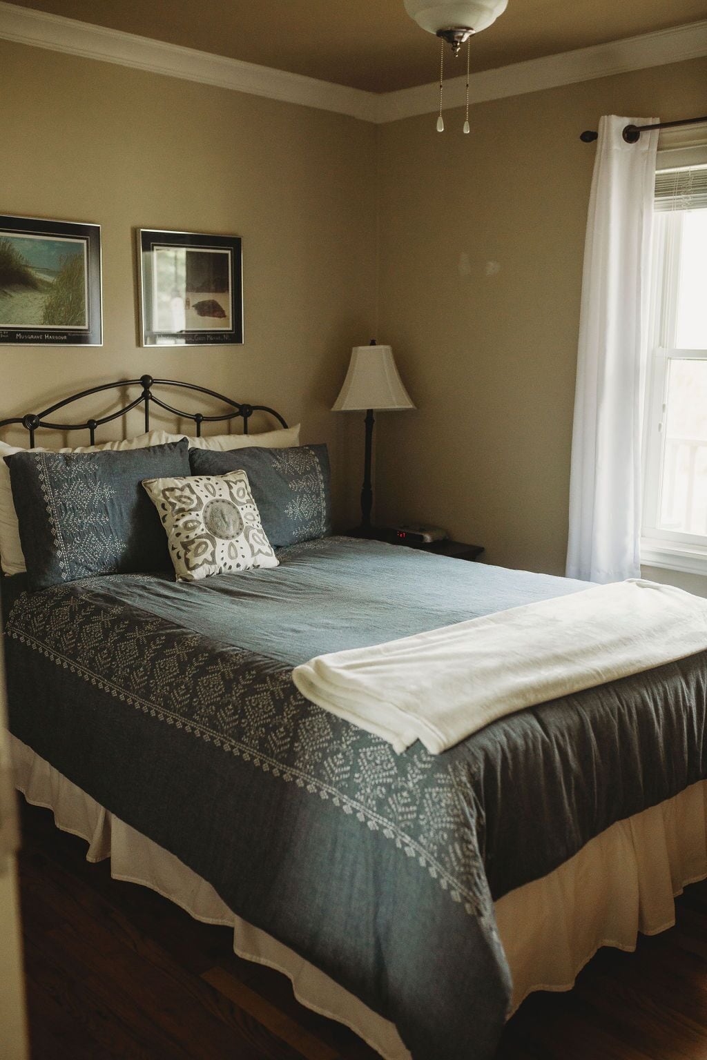 A neatly made bed with a patterned bedspread and pillows, a bedside lamp, and framed pictures on the wall.