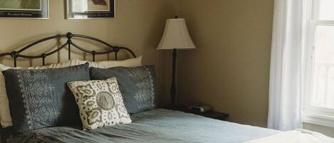 A neatly made bed with a patterned bedspread and pillows, a bedside lamp, and framed pictures on the wall.