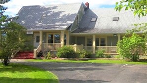 A two-story house with a front porch, a covered driveway, and a small front yard. - The Carriage House Inn (Grand Falls - Windsor)
