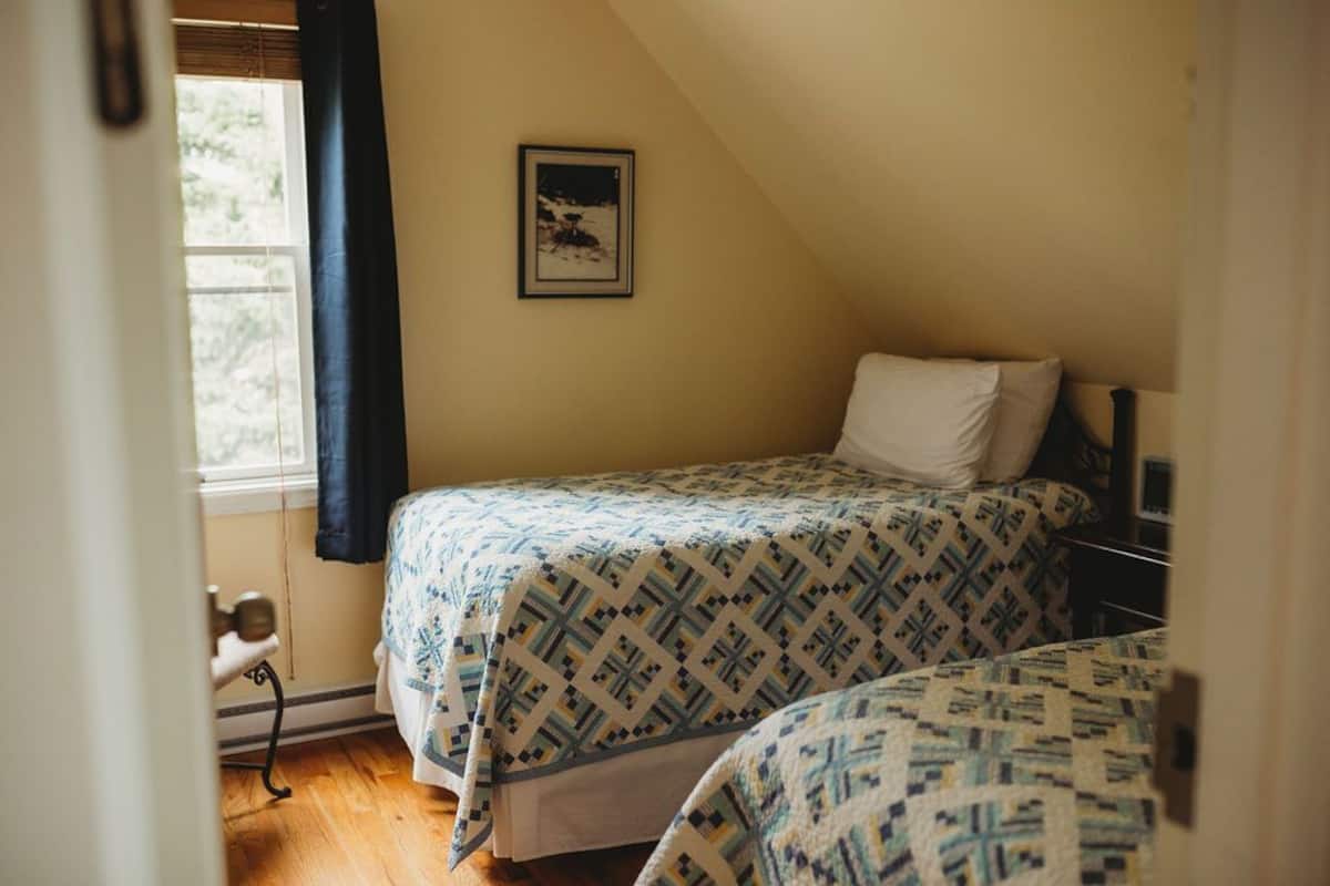 A bedroom with two beds, a window with curtains, a framed picture on the wall, and a wooden floor.