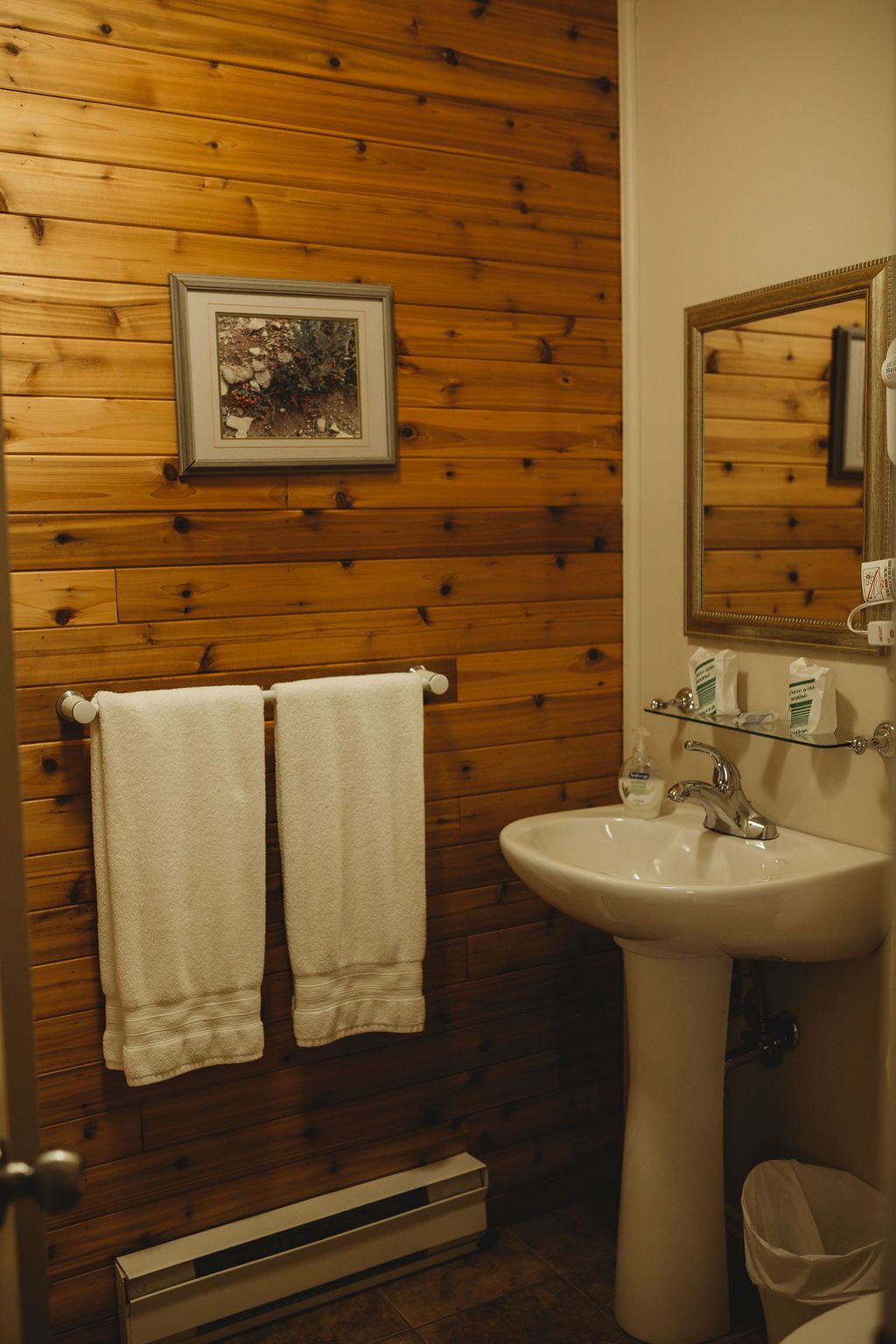 Un baño con paneles de madera, un lavabo blanco, un espejo y dos toallas colgadas en un perchero.
