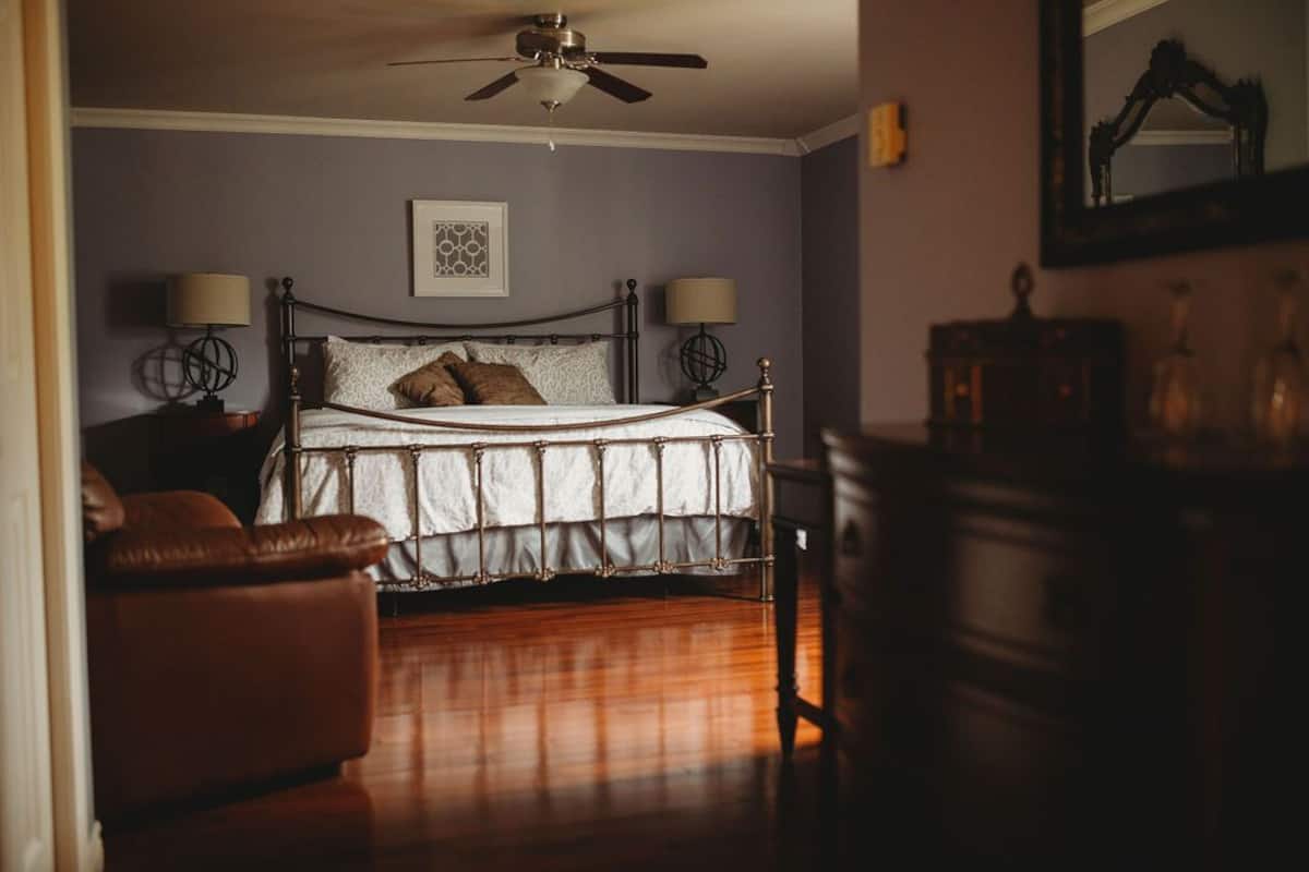 A bedroom with a bed, two bedside lamps, a ceiling fan, a framed picture on the wall, and a wooden dresser.