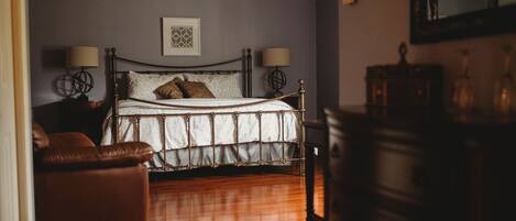 A bedroom with a bed, two bedside lamps, a ceiling fan, a framed picture on the wall, and a wooden dresser.