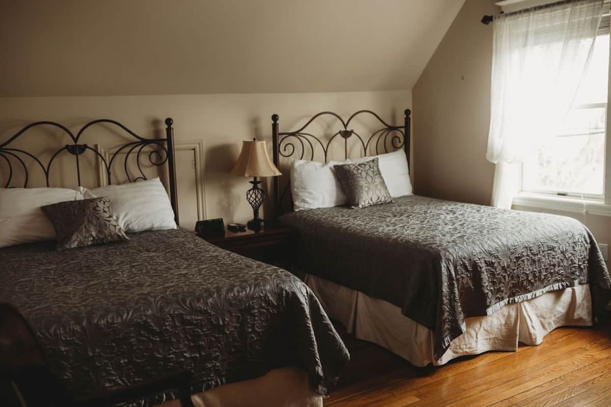 A bedroom with two beds, a nightstand, a lamp, and a window with sheer curtains.