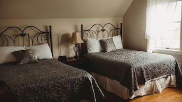 A bedroom with two beds, a nightstand, a lamp, and a window with sheer curtains.