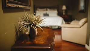 A bedroom with a bed, a bedside table with a plant, and a nightstand with a lamp. - The Carriage House Inn (Grand Falls - Windsor)