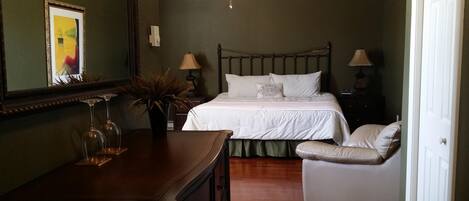 Une chambre à coucher comprenant un lit, des lampes de chevet, une chaise, une commode, un miroir et un ventilateur de plafond.